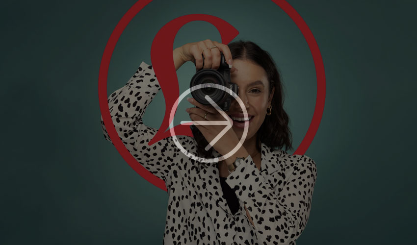 Person in a black-and-white polka dot shirt holds a camera against a teal background with a red pattern.