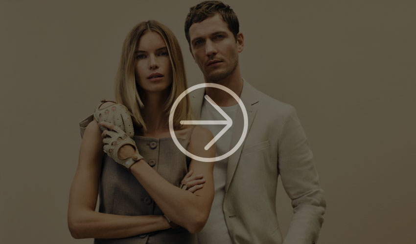 Stylish couple poses in chic outfits against a beige background, with artistic lighting effects.