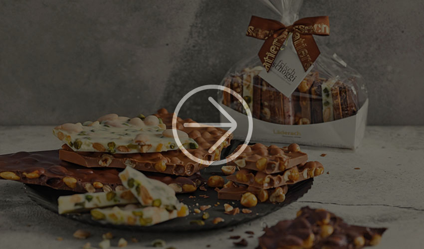 Broken chocolate with nuts on a black plate, next to a wrapped treat with a bow.