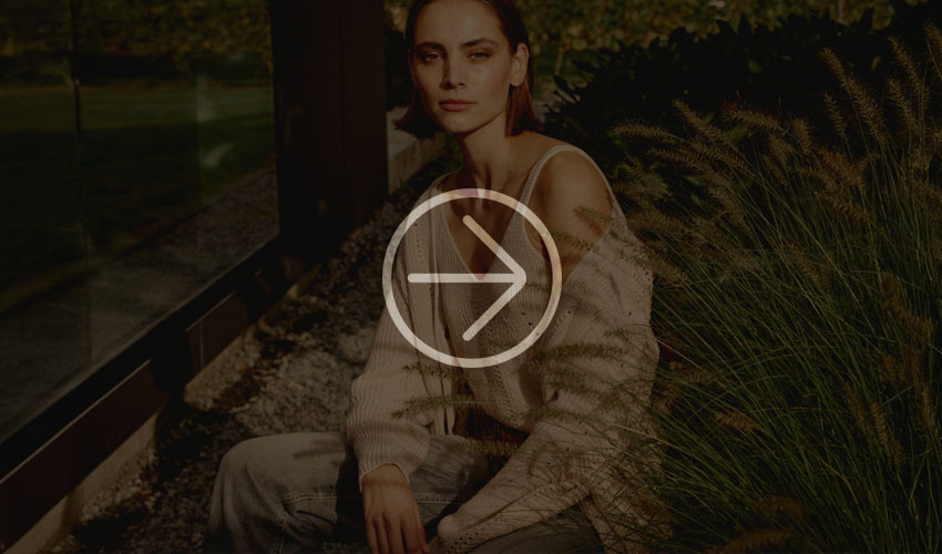Woman in a knitted sweater sits in the grass near a modern building, illuminated by sunlight.