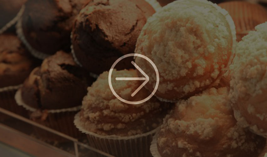 A close-up of chocolate and sprinkle-coated muffins displayed in a bakery display case, highlighting their texture and deliciousness.