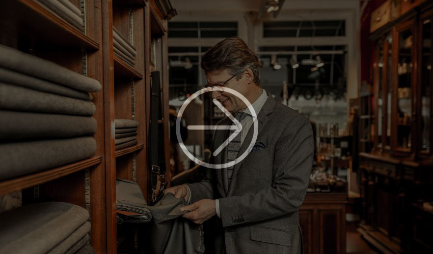 Well-dressed man examines fabric samples in an elegant store with shelves full of textiles.
