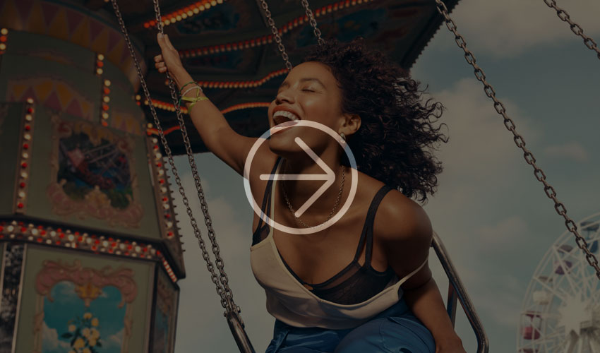 Person swinging happily on an amusement park ride, surrounded by bright colors and vintage decorations.