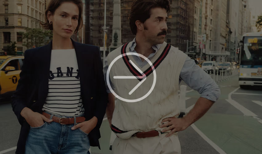 A stylish couple in trendy outfits on a busy city street, with a taxi and bus in the background.