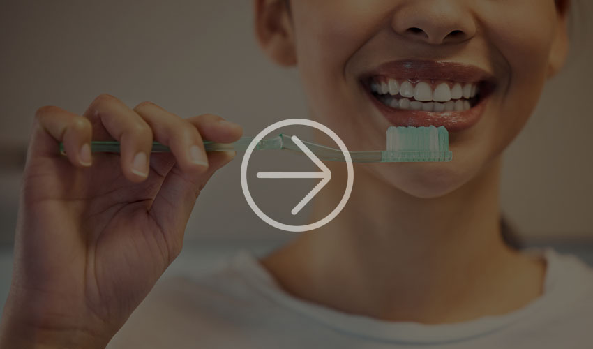Close-up of a smiling woman holding a toothbrush with toothpaste and ready to brush her teeth to promote dental hygiene.