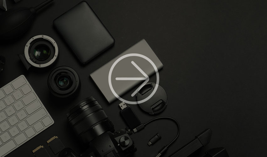  Flat arrangement of photographic equipment, including lenses, a camera, a keyboard, portable memory and a battery pack on a black surface.