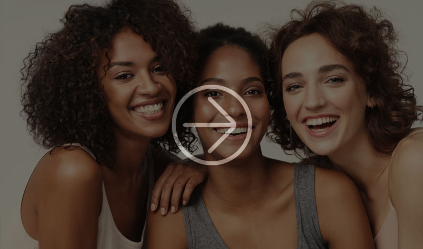 Three young women smile happily at the camera, leaning on each other.