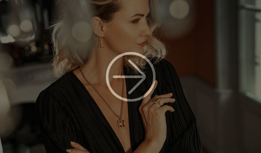 Stilvolle Person mit elegantem Schmuck posiert und präsentiert Goldkette und Ringe vor sanftem Hintergrund.