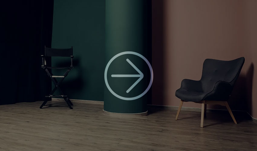 Modernes Interieur mit schwarzem Regiestuhl und dunkelgrauem Sessel vor grün-rosa Wänden.