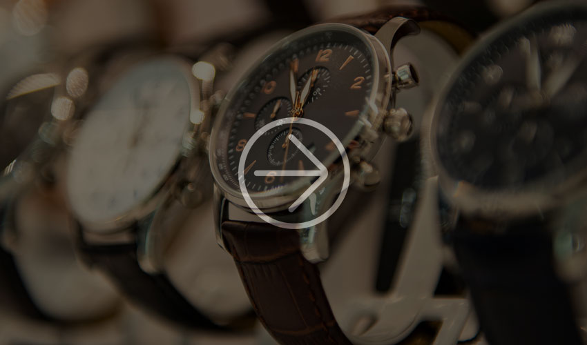 Nahaufnahme einer Armbanduhr mit schwarzem Zifferblatt, braunem Lederarmband und weiteren Zeitmessern.