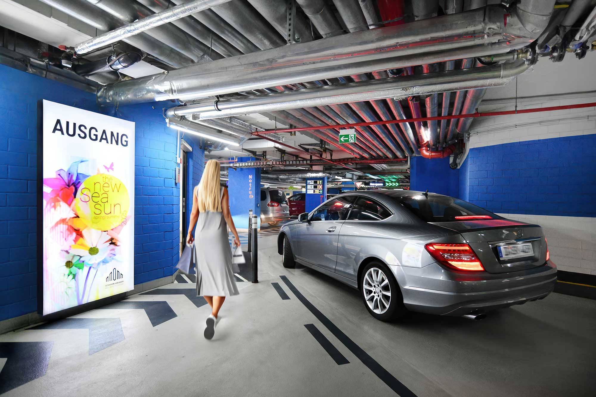 Frau läuft mit Einkaufstüten in der Hand in der Tiefgarage neben einem Auto entlang