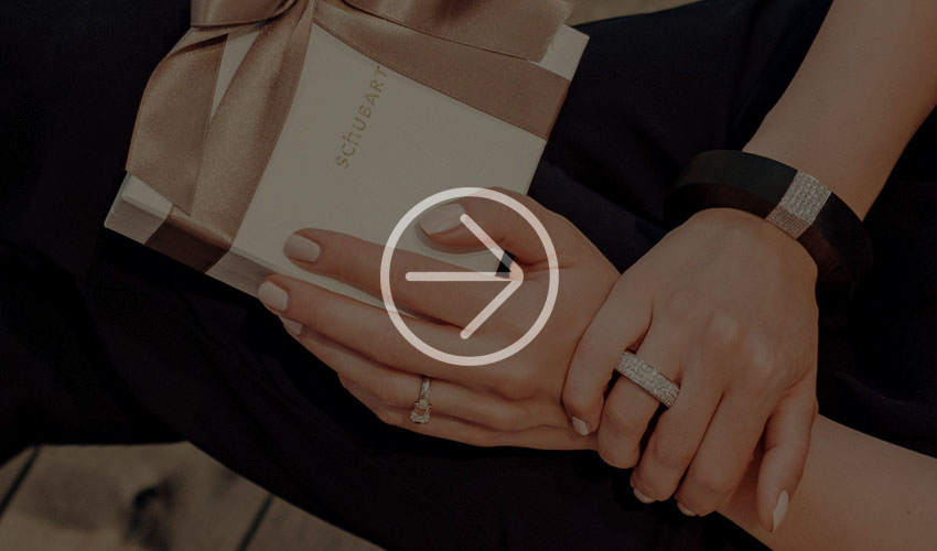Nahaufnahme manikürter Hände, die eine Geschenkbox mit Diamantringen und einem Armband halten.       