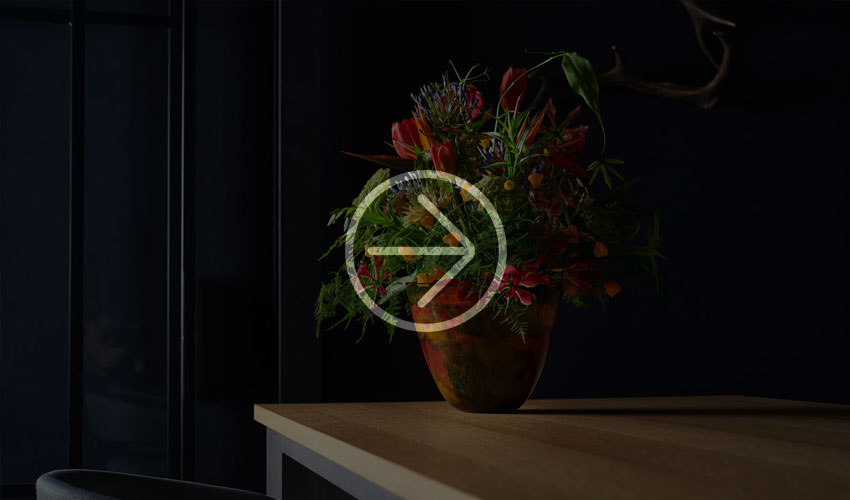 Farbenfrohes Blumenarrangement in rustikaler Vase auf Holztisch vor dunklem Hintergrund.        