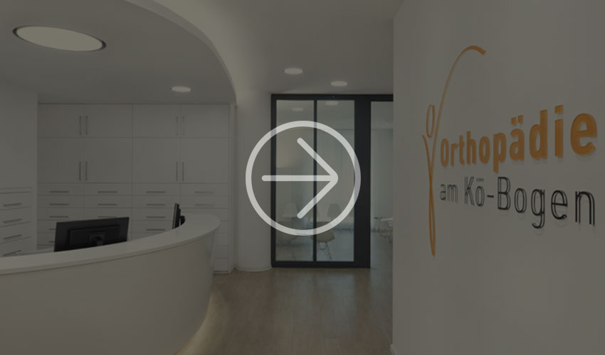  Bright, modern reception area of an orthopaedic clinic with curved desk and orange signage as well as glass doors leading to the patient areas.